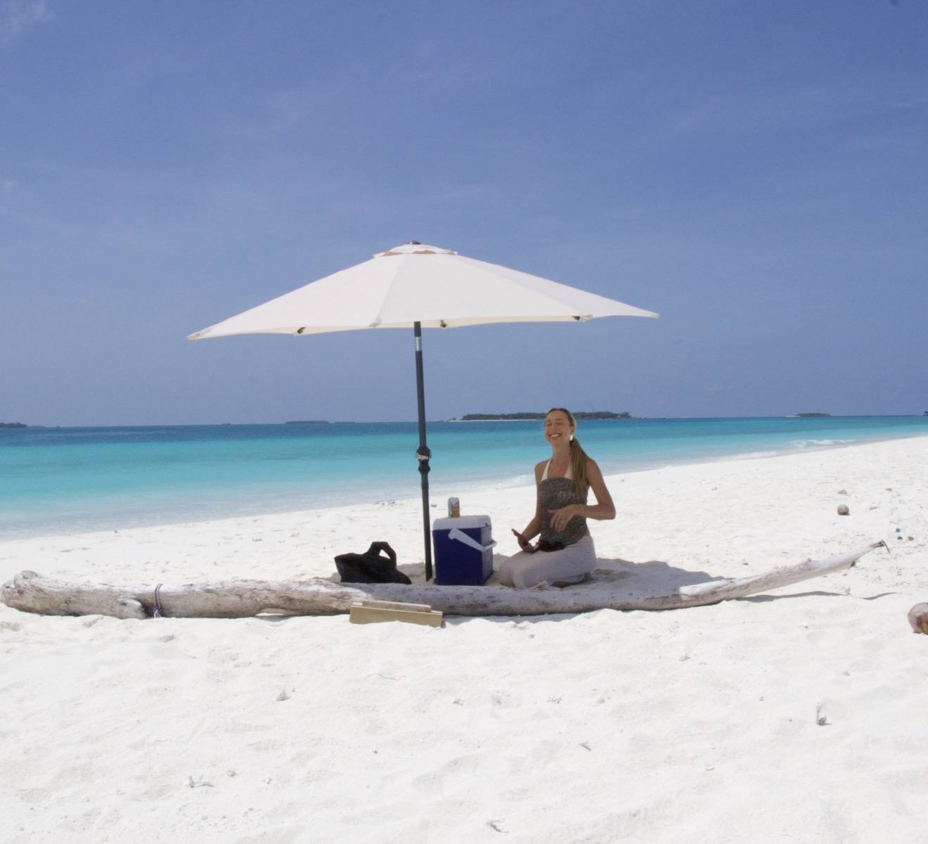 A white umbrella and a picnic set up on an empty sandbank
