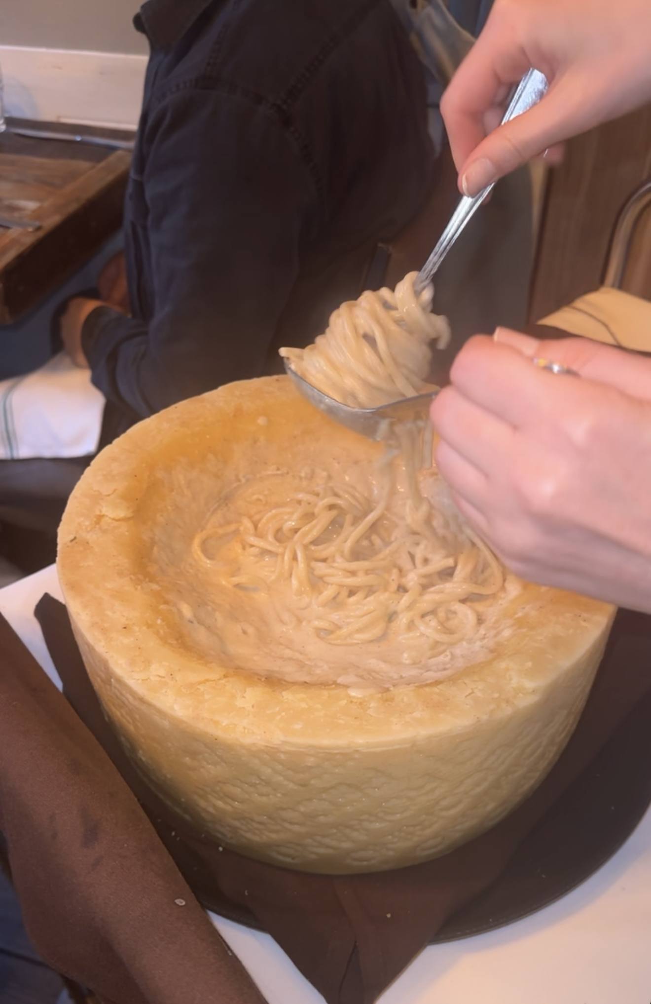 Pasta being tossed inside a hollowed wheel of pecorino at the table