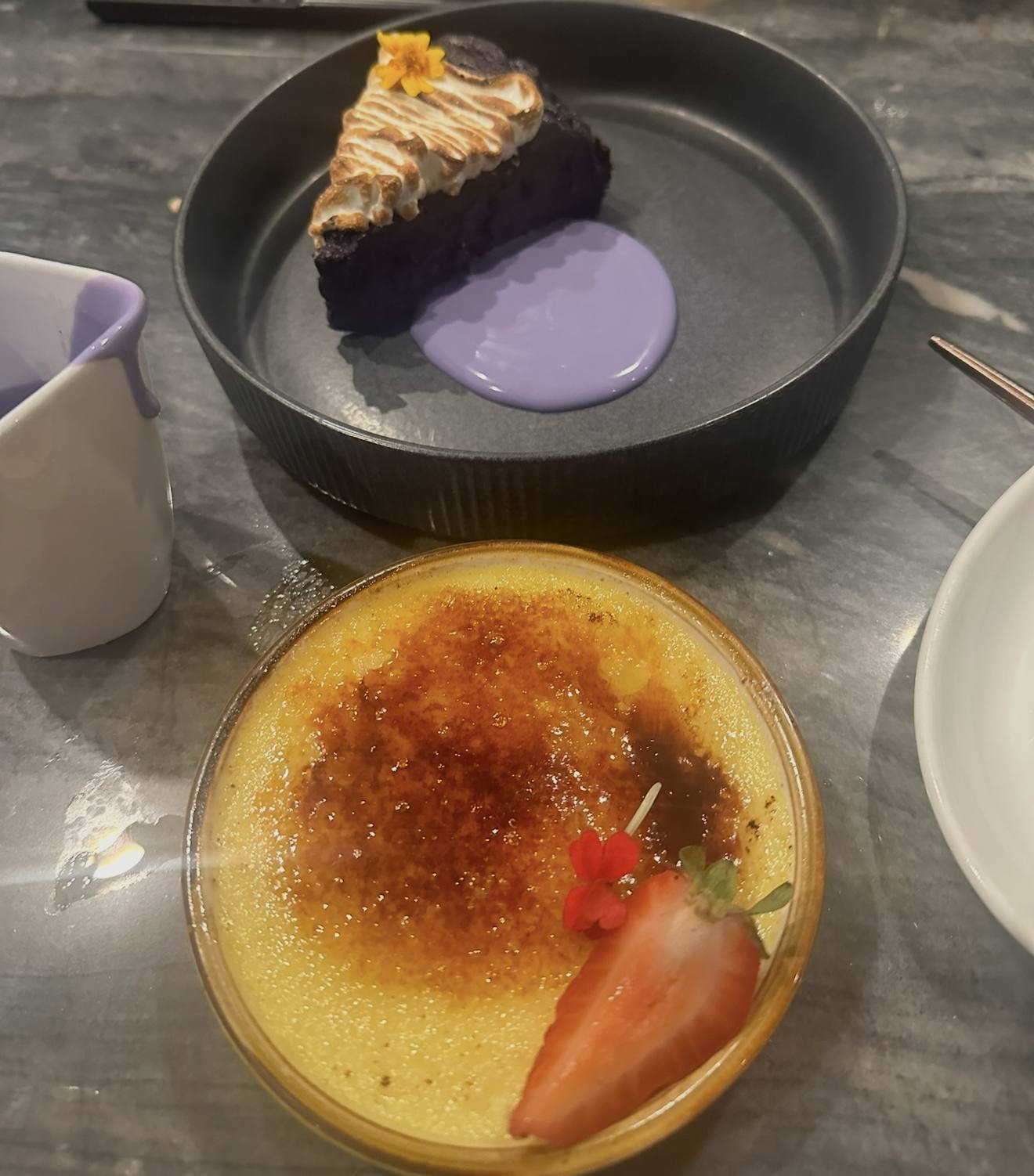 Two desserts on dark plates, a crème brûlée and a tart