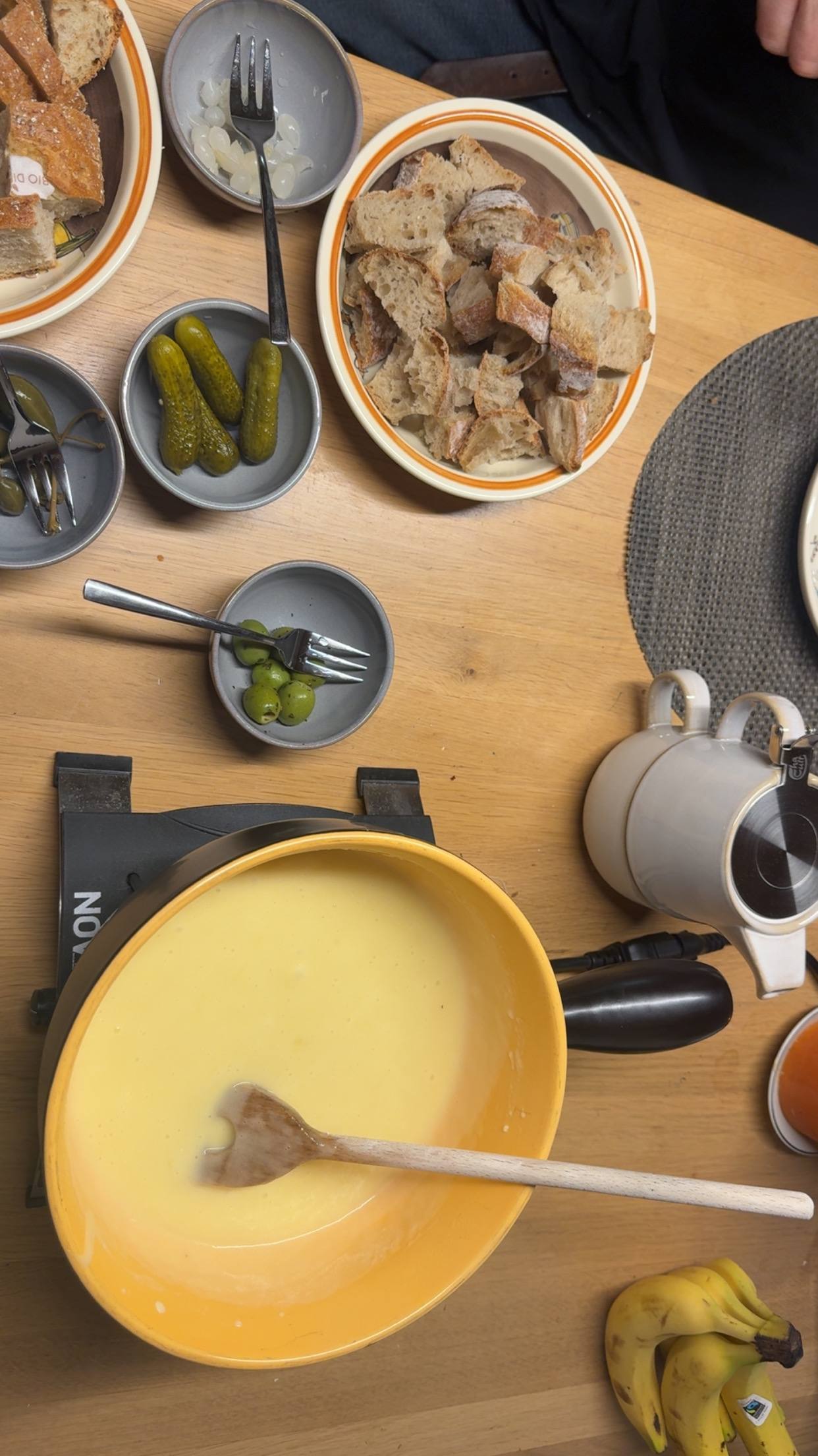 A fondue table laid with a cheese pot, pickles and boards