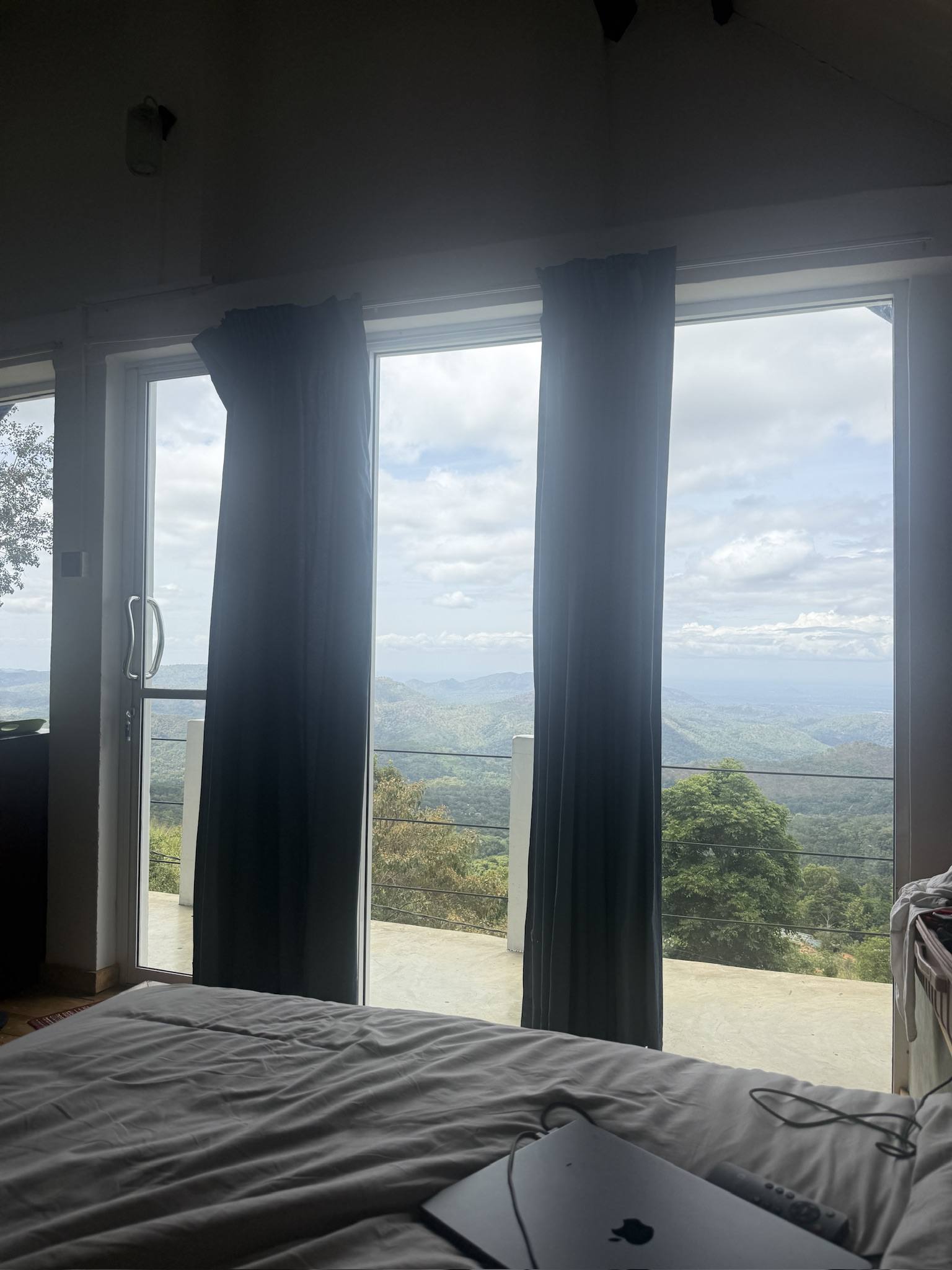 A bedroom with floor-to-ceiling windows looking over green hills