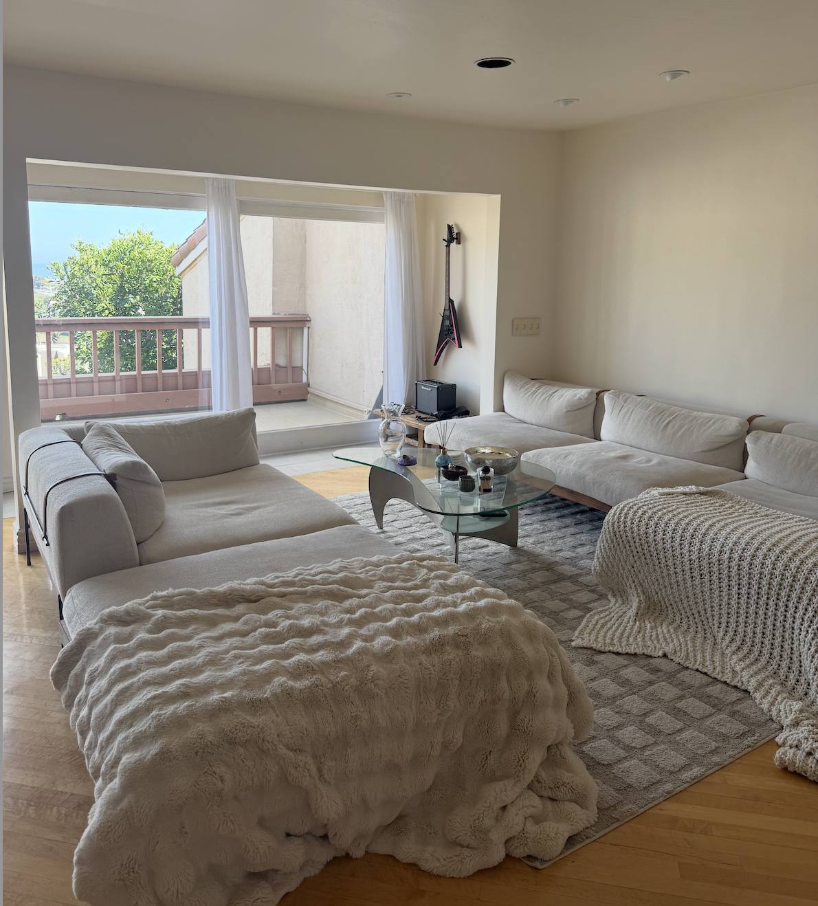 Two facing cream sofas with a kidney-shaped glass coffee table on a checkerboard rug, doors open to the balcony