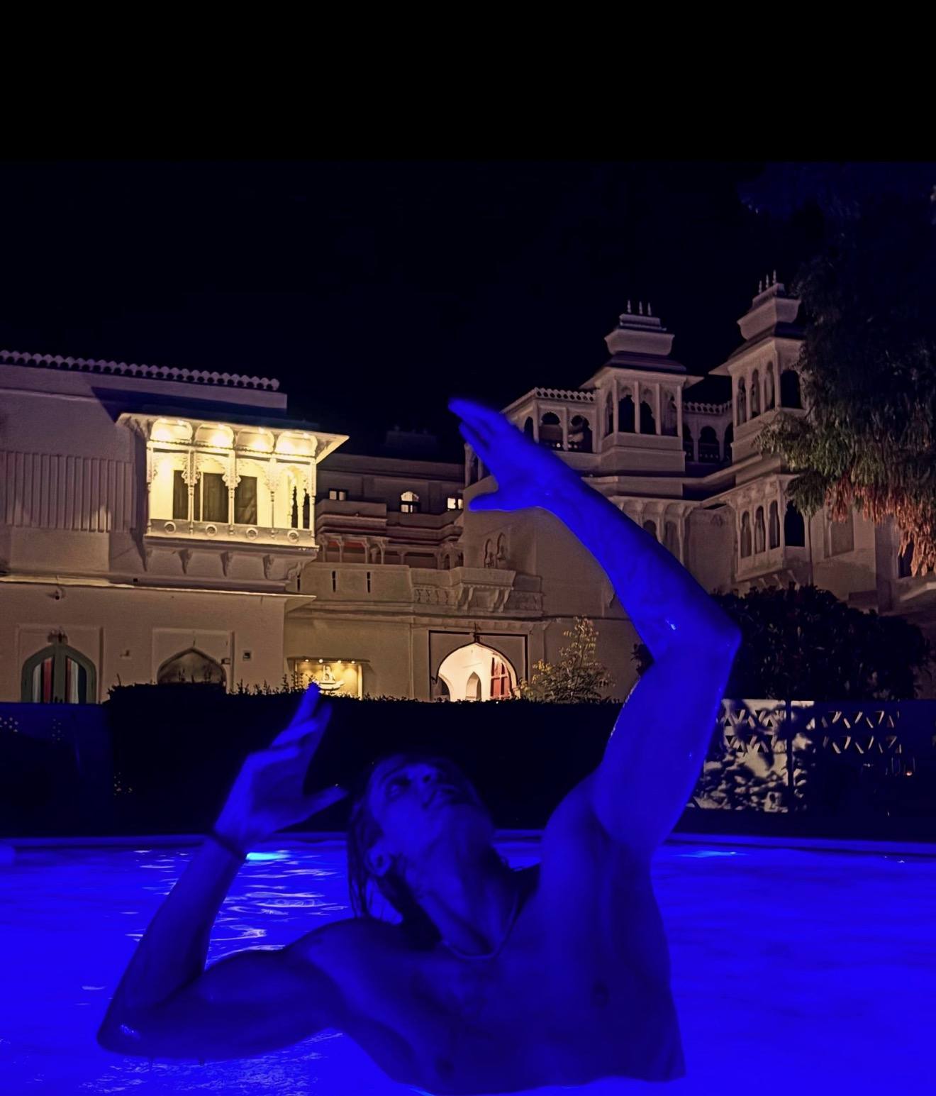 Swimming at night in a lit pool below a floodlit palace