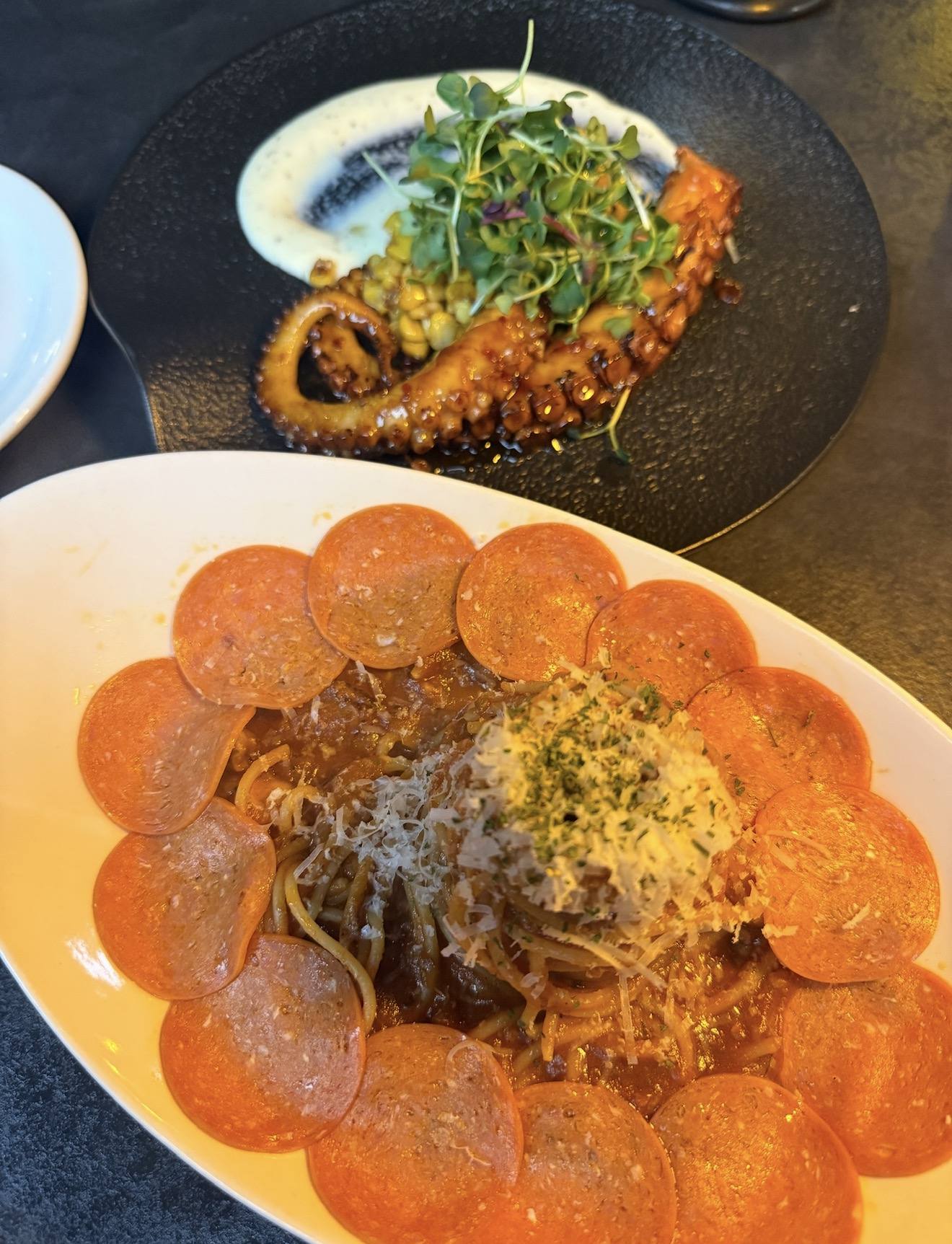 A plate of pasta ringed with pepperoni beside grilled octopus