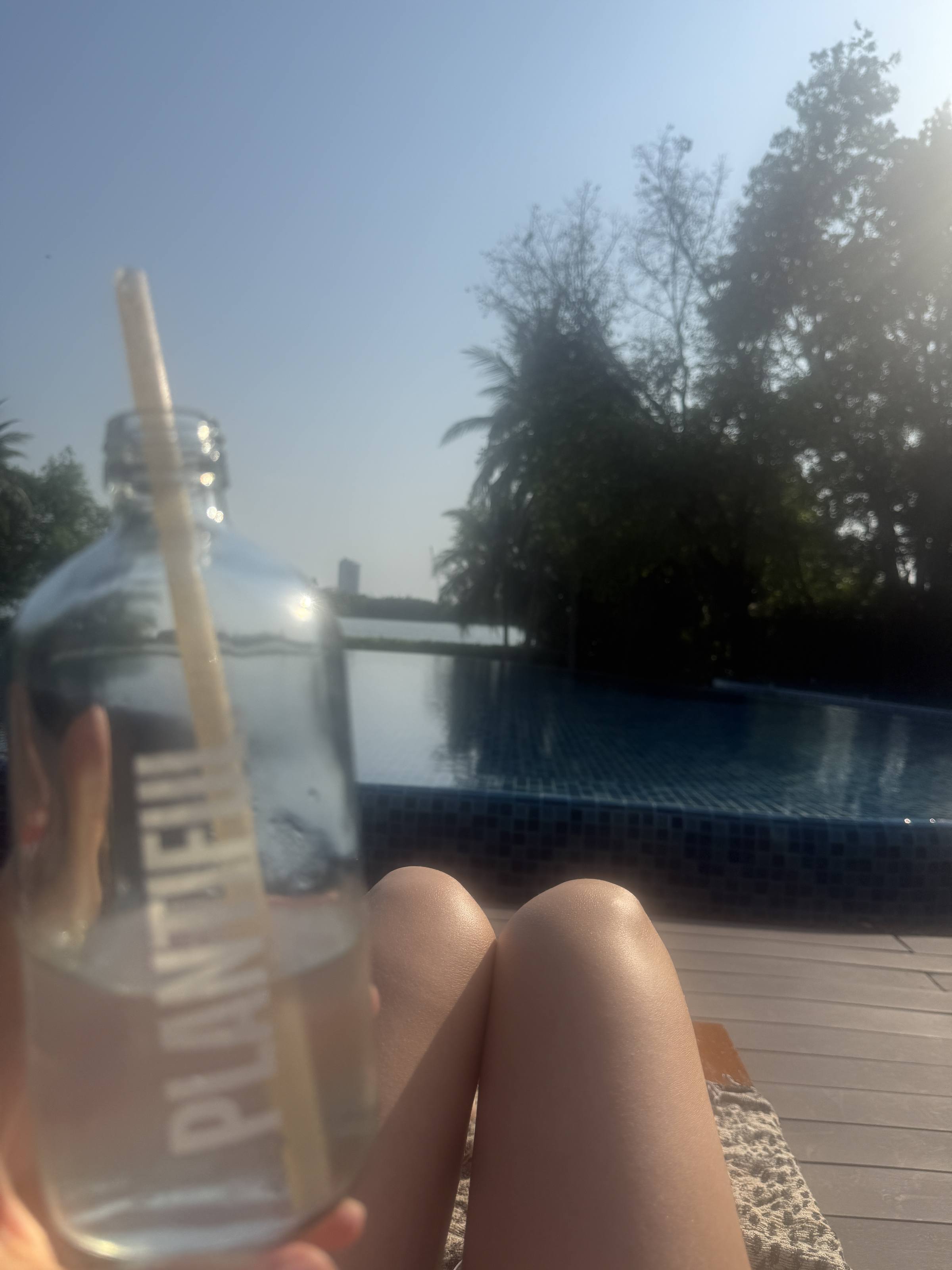 A clear bottled drink held up in front of a pool