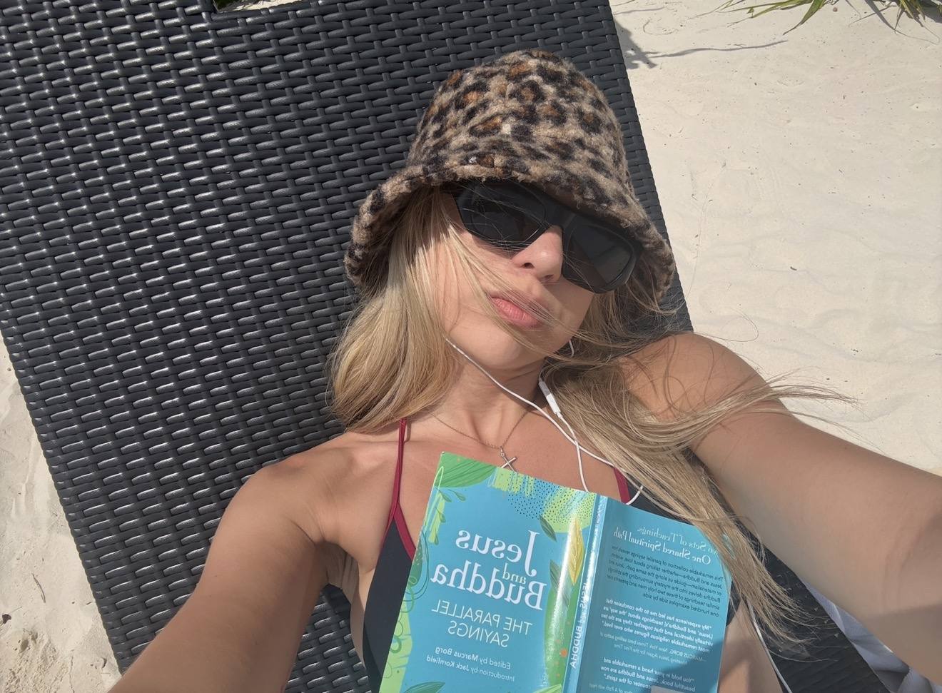 Reading on a sun lounger in a leopard bucket hat and sunglasses